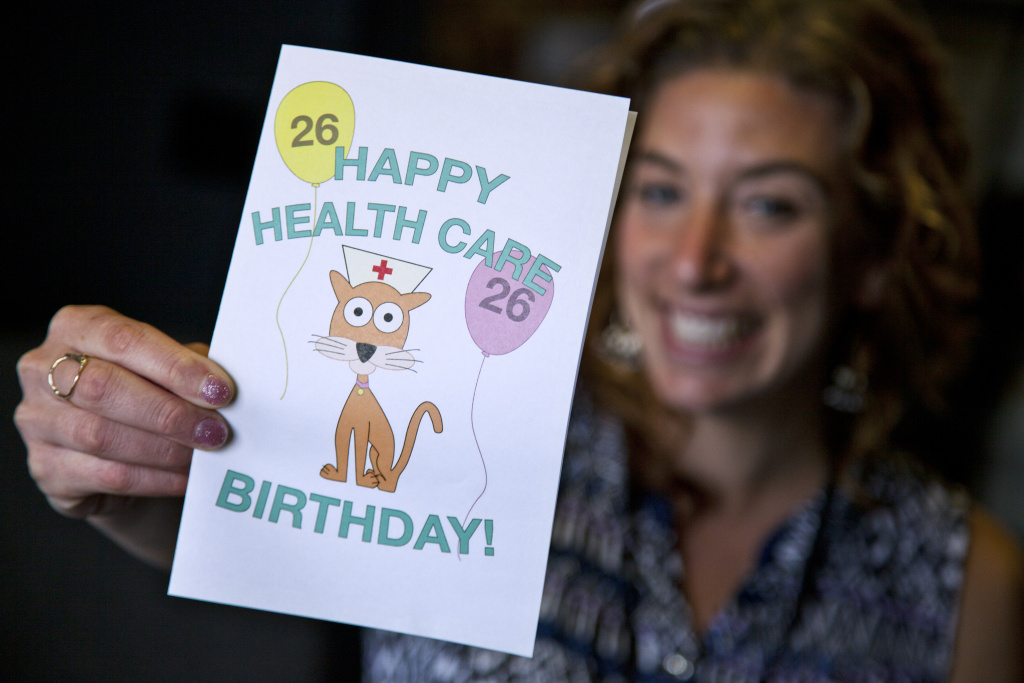 woman holding a 26th birthday card that says Happy Health Care Birthday with balloons marked 26