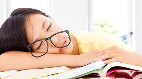 young girl asleep at her desk on top of a pile of books